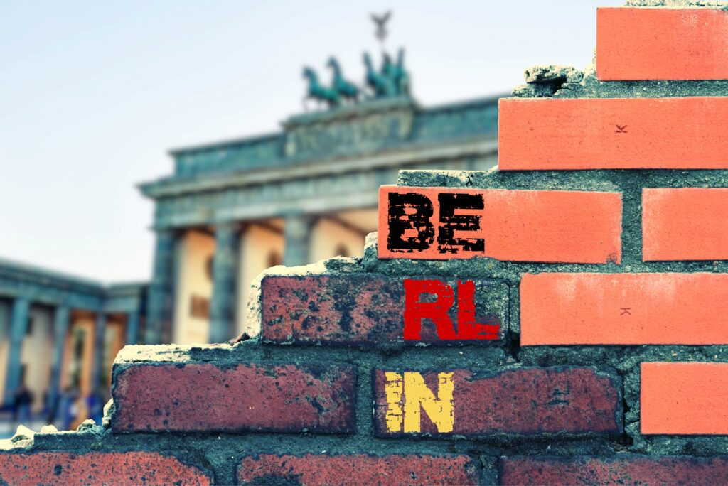 Klassenfahrt Berlin: Backsteinmauer mit Schriftzug „Berlin“ und Blick auf das Brandenburger Tor