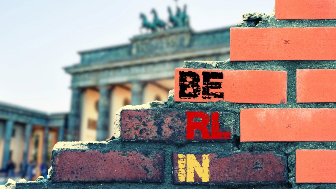 Klassenfahrt Berlin: Backsteinmauer mit Schriftzug „Berlin“ und Blick auf das Brandenburger Tor