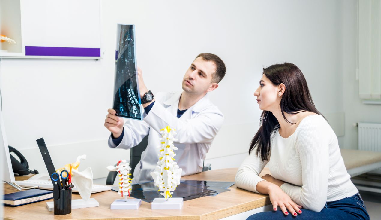 Orthopäde Köln erklärt einer Patientin ein Röntgenbild der Wirbelsäule im Behandlungsraum